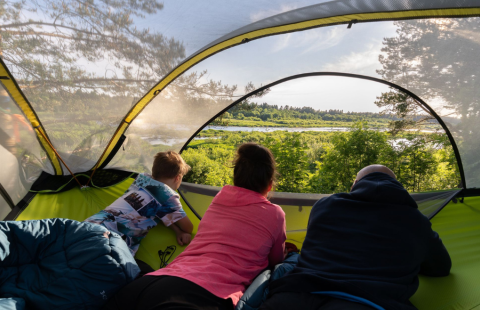 Kolme henkilöä makaamassa avoimessa teltassa ja katselemassa maisemia.